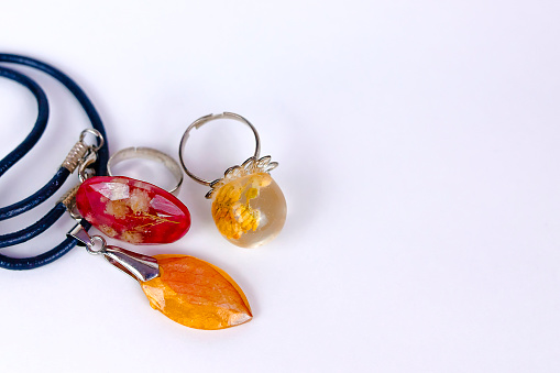 pendant and rings with dried flowers inside crystals made of epoxy resin on white background. Close-up shallow depth of field. Handmade, DIY bijouterie flat lay