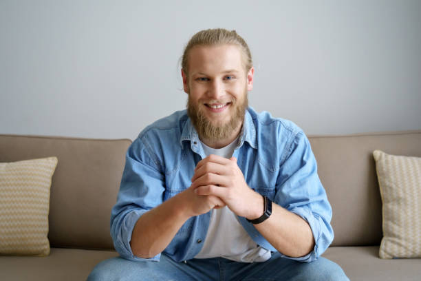 istock Smiling millennial hipster guy blogger looking at camera video calling, recording vlog. Happy young man distance chatting at home office, streaming sitting on sofa. Headshot portrait. Webcam view 1220135111