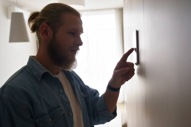 istock Young man using smart touch screen technology connected appliances device on wall monitoring energy security system digital control set comfort house room heating thermostat app, smart home concept. 1220135167