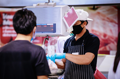 butcher holding piece of fresh red raw meat in hands showing meat, bowl from refrigerator on scales in supermarket.covid-19 spreading outbreak