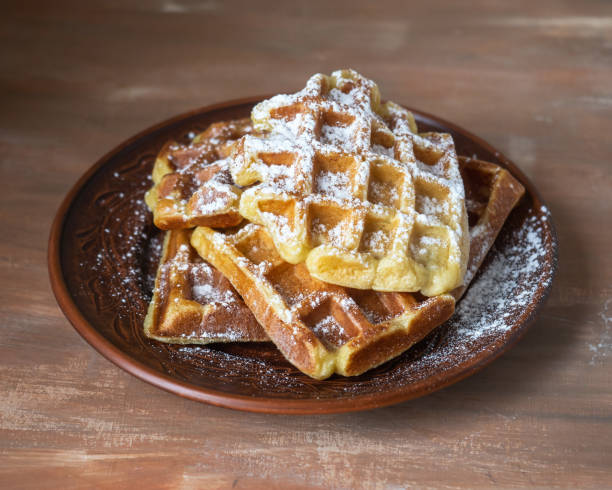 istock Sweet dessert. Homemade waffles with icing sugar slide on a table in a brown ceramic plate on a brown table 1220141593