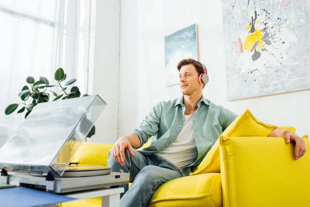 istock Handsome man in headphones sitting on couch near record player on coffee table 1220142241