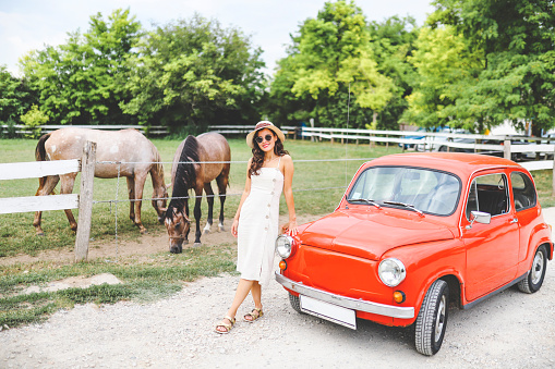 Fashion woman and red vintage car on horse's farm