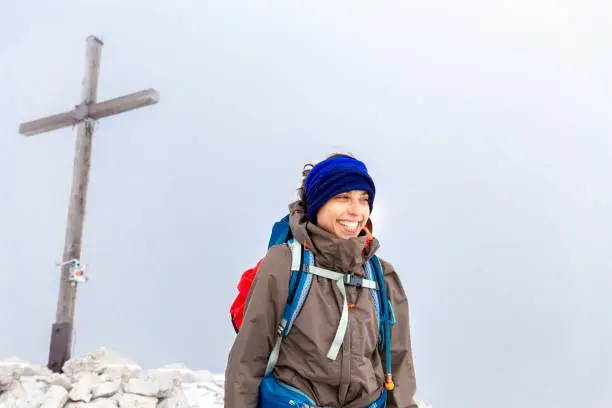 Young happy smiling laughing woman backpacker tourist standing alone mountain summit peak christian cross, looking scenic landscape view, South Tyrol alps travel Italy alone Europe tourism.