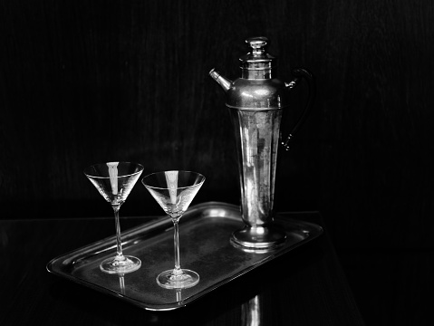 Black and white image of cocktail glasses and antique silver decanter claret jug on a silver plate.
