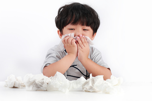 Little Asian Girl Sneezing and Blowing Nose With Tissue Against White Background