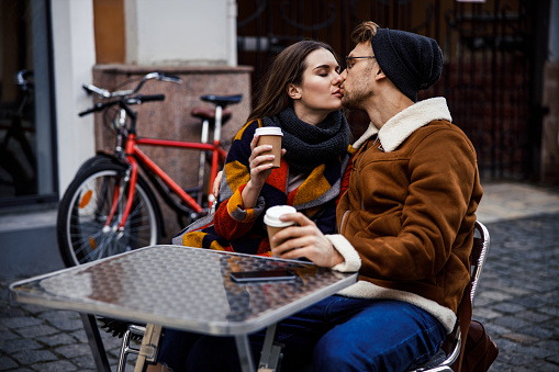 Romance between two young people. Man and woman kissing wit closed eyes and holding cups of coffee