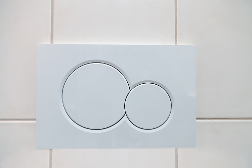 Economic white dual buttons of flush toilet bowl on tiled wall in bathroom. Flushing system in closet