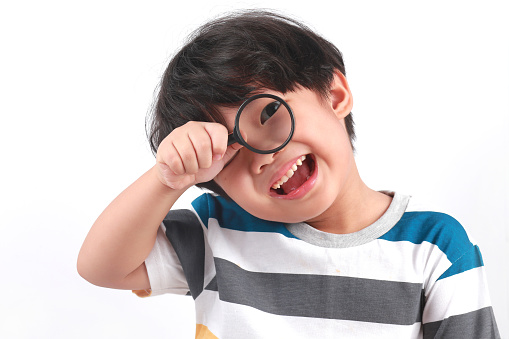 Portrait of little Asian boy using magnifying glass against white background