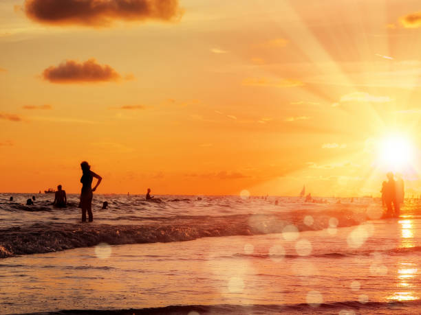 large group of silhouetted people on public beach over orange colored sunset sky in Siesta key, Sarasota, Florida