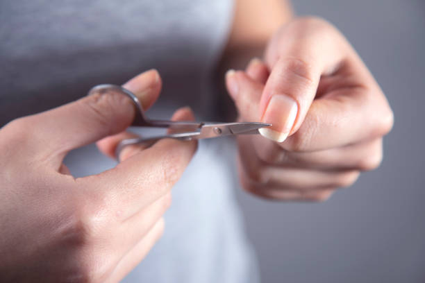 woman cut the nail with scissors on grey background
