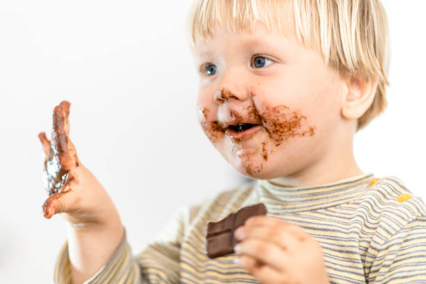 istock Cute blond dirty toddler eating chocolate bar with great pleasure 1220160421
