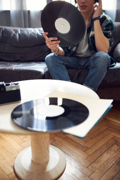 istock Young man sitting on couch and holding vinyl record 1220161506