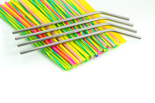 Reusable stainless steel straws above disposable plastic straws on a white background. Zero waste concept. Copy space.