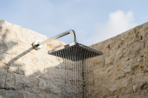 Close up of water flowing from turned on shower head in modern bathroom interior with open space and sky over walls