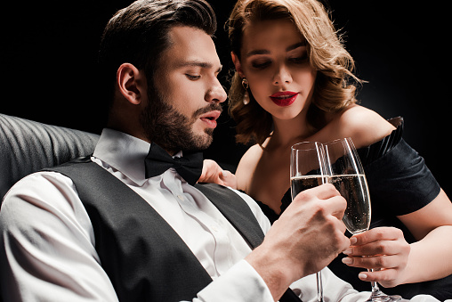 attractive woman and elegant man clinking glasses of champagne isolated on black