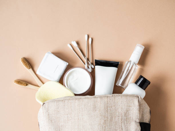 Travel cosmetic bag with the necessary means to care for women's skin. Cosmetics, dry shampoo, cotton buds, toothbrushes next a cosmetic bag on a beige background. top view stock photo