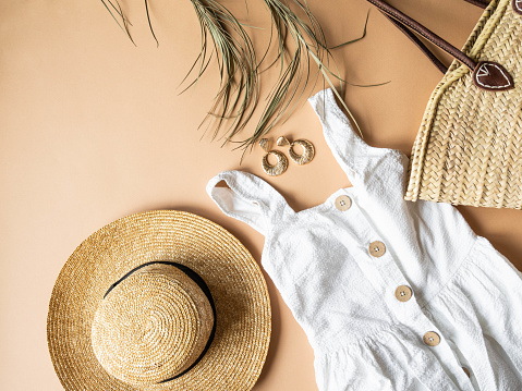 Women's summer straw hat, wicker bag, white sundress, sunglasses and jewelry on beige background. Copy space. Top view