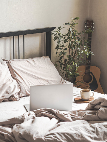 Laptop and coffee on the bed and a guitar next to the bed in the bedroom. Work from home or a comfortable pastime online. Stay home, quarantine. Work at home concept.