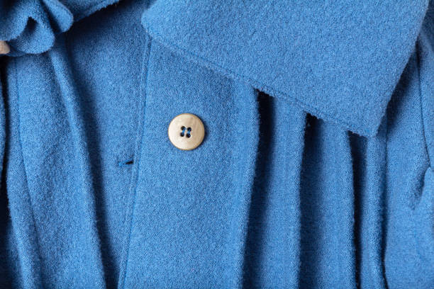 Fragment of a button and collar with folds of a fashionable blue woolen coat Blue wool texture of a thin Italian pleated coat with a close-up collar and button. Concept of children's and women's fashion and clothing Atelier coat wool button clothing stock pictures, royalty-free photos & images