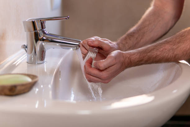 istock Caucasian man thoroughly cleaning hands and fingernails with a brush in wash basin under running water tap. Personal hygiene as coronavirus COVID-19 pandemic spread prevention. 1220168181