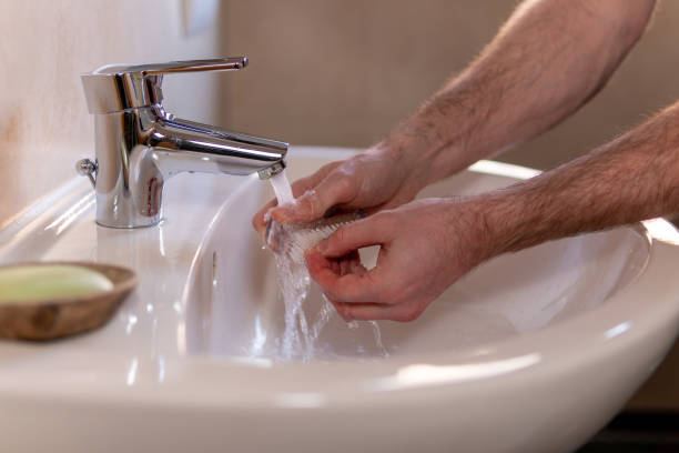 istock Caucasian man thoroughly cleaning hands and fingernails with a brush in wash basin under running water tap. Personal hygiene as coronavirus COVID-19 pandemic spread prevention. 1220168758