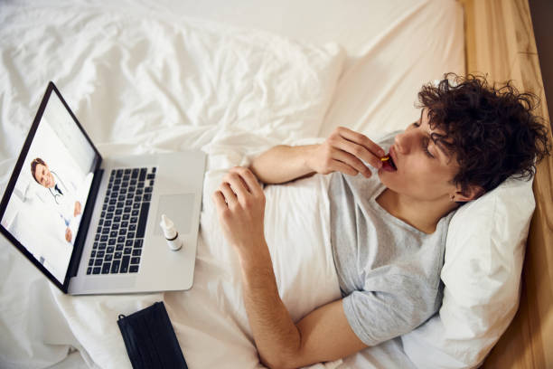 istock Sick young man taking pill while having online consultation with doctor 1220168875