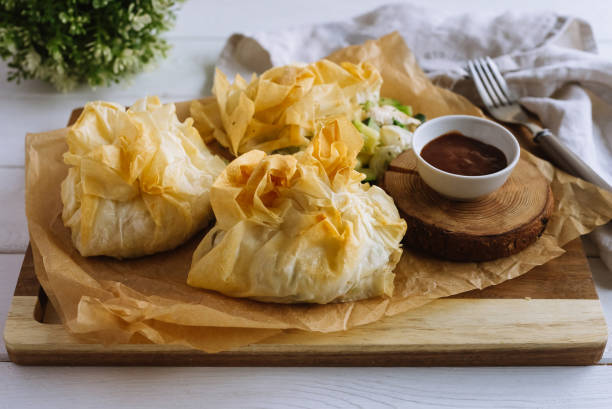 Filo pastry pouches filled with chicken and vegetables on a cutting board with barbecue sauce. On a white wooden table with a kitchen towel. filo pastry stock pictures, royalty-free photos & images