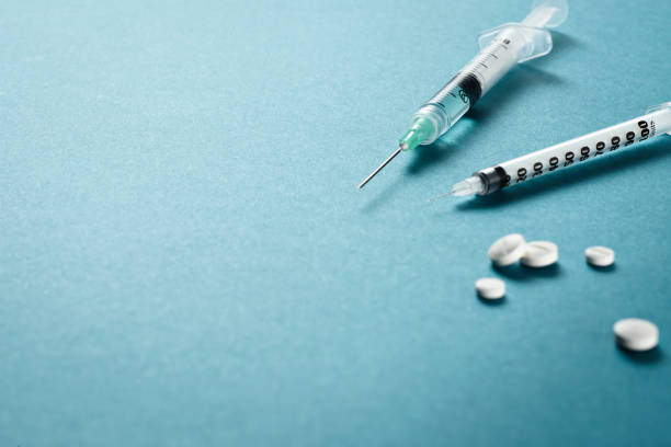 istock Syringes with needles among tablets or medicine pills and medicine pack on a green surface. Perfect for pharmaceutical or medical purposes, fighting a pandemic or symptoms of a flu or disease. 1220169864