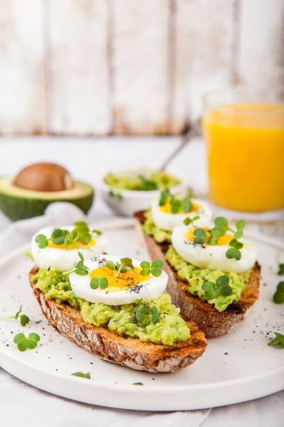 Tasty sandwich with avocado, microgreen and poached egg on grey board, close up, selective focus. Healthy delicious breakfast or lunch