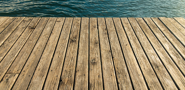 A weathered jetty dock - with an open row boat tied to one of its double cleat mooring bollards - is floating peacefully at water's edge on a harbor bay or lake in Nova Scotia, Canada.