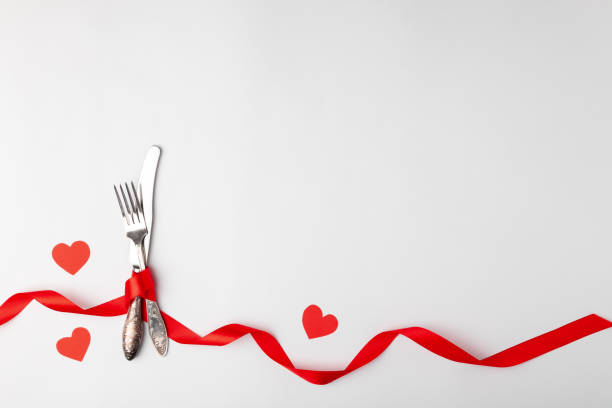 istock Anniversary, birthsday festive romantic table setting on white background. Silverware, vintage fork, knife with red ribbon, paper hearts. Place for text, copyspace, top view 1220173000