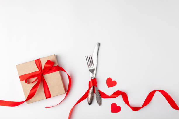 istock Romantic setting on white background. Valentines day card template. Kraft gift box with red ribbon, paper hearts, silverware. Concept anniversary, mother birthday, place for text, copyspace, top view 1220173058
