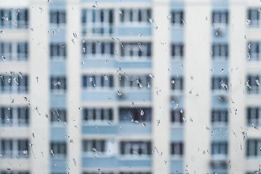Dirty rainy window overlooking residential buildings, water drops on a glass. Self isolation concept, loneliness, sad mood