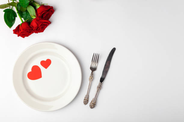 istock Valentines day dinner with festive table setting, red roses, tape, hearts, ceramic plate, vintage silverware on white background. Top view, space for text, copy space, birthday greeting, anniversary 1220173346