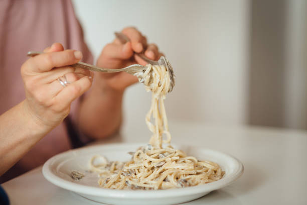 istock Young woman eats Italian pasta with mushrooms. Close-up spaghetti winds it around a fork with a spoon 1220173413