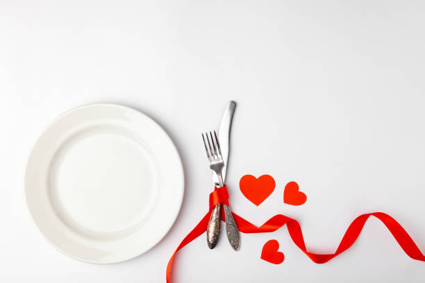 istock Romantic festive table setting on white background. Valentines day card template. Red ribbon, plate, silverware, vintage fork, knife. Concept anniversary, birthday, place for text, copyspace, top view 1220173433