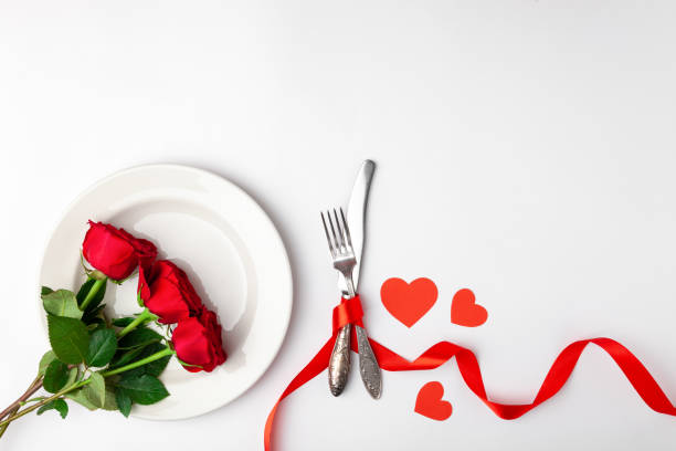 istock Valentines day dinner with festive table setting, red roses, tape, hearts, ceramic plate, vintage silverware on white background. Top view, space for text, copy space, birthday greeting, anniversary 1220173468