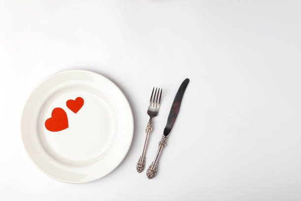 istock Romantic festive table setting on white background. Valentines day card template. Red paper hearts in ceramic plate, silverware, vintage fork, knife. Place for text, copyspace, top view 1220173500