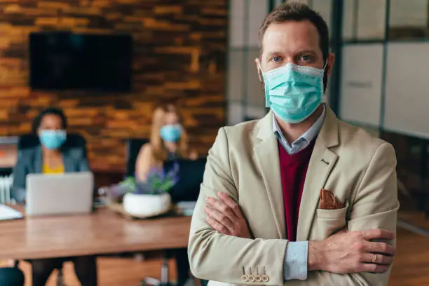 Businesspeople wearing masks in the office for illness prevention during COVID-19 pandemic, portrait of businessman with arms crossed