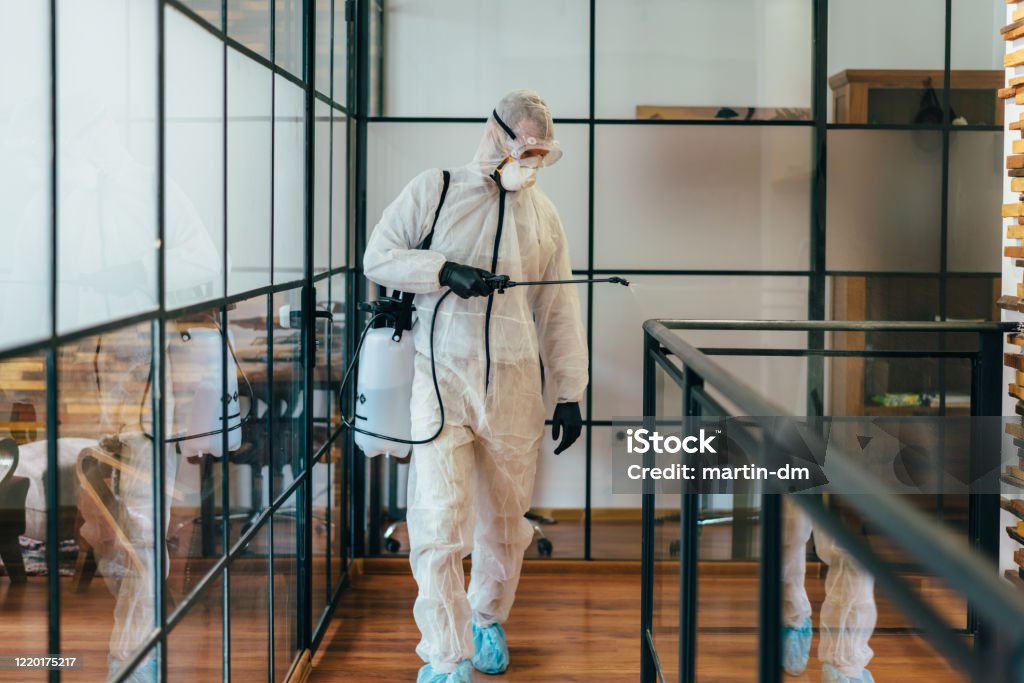 Office disinfection during COVID-19 pandemic Man in protective suit and face mask spraying for disinfection in the office Disinfection Stock Photo