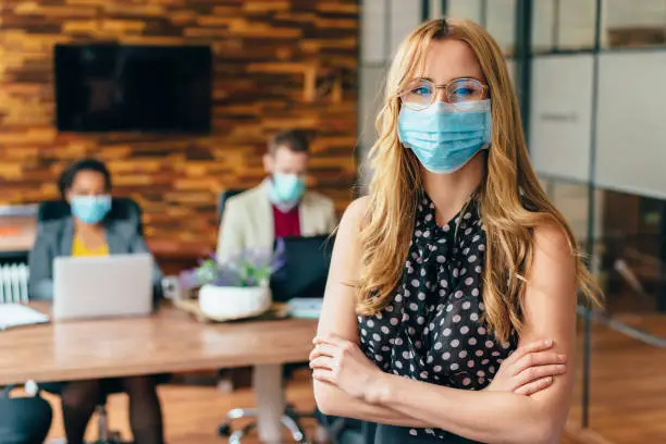 Businesspeople wearing masks in the office for safety during COVID-19 pandemic, young businesswoman looking at camera