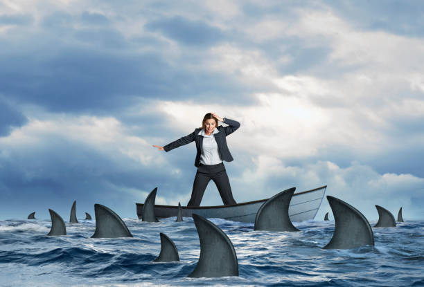 istock Stranded Businesswoman Surrounded By Sharks in Dinghy 1220175473