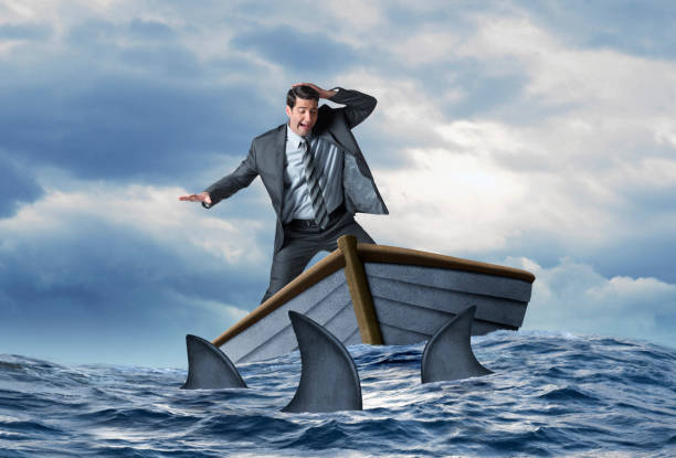 istock Stranded Businessman Surrounded By Sharks in Dinghy 1220175477