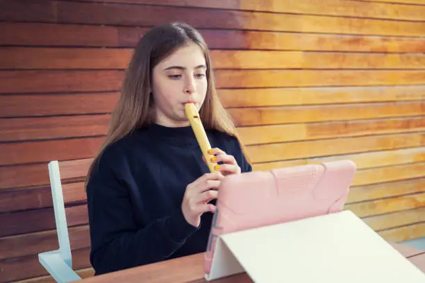 Teenager playing flute at home teleconferencing with music friends using a tablet pc