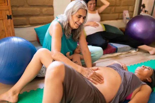 Beautiful mature doula with grey hair examines a pregnant woman