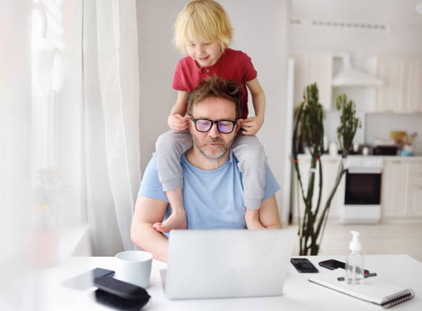 istock Man working from home with laptop during quarantine. Home office and parenthood at same time. Exhausted parent with hyperactive child. 1220178027