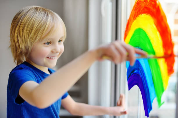 istock Little boy drawing on window rainbow while coronavirus quarantine. Rainbow sign is symbol of hope, means that everything will be OK. 1220178068