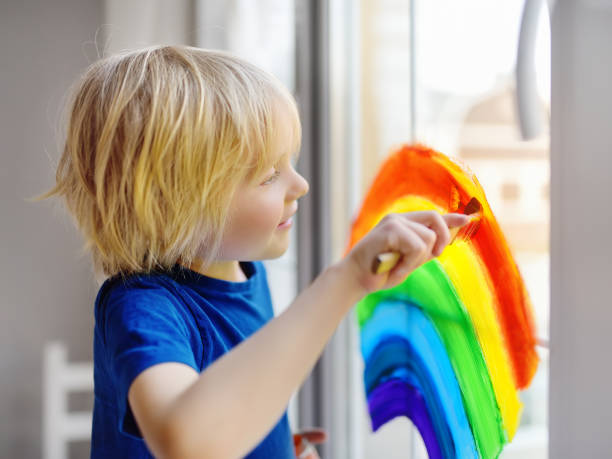 istock Little boy drawing on window rainbow while coronavirus quarantine. Rainbow sign is symbol of hope, means that everything will be OK. 1220178082