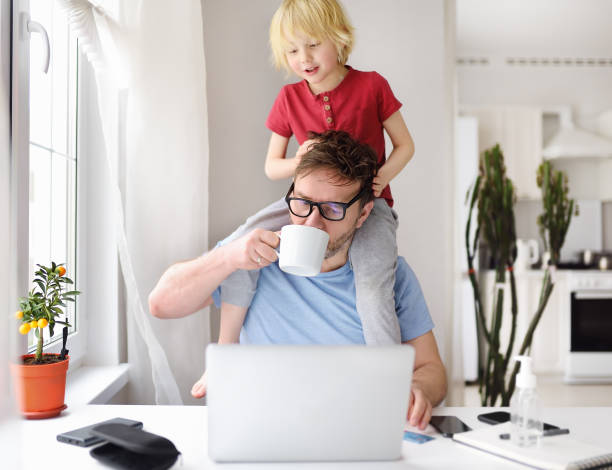 Man working from home with laptop during quarantine. Home office and parenthood at same time. Exhausted parent with hyperactive child.